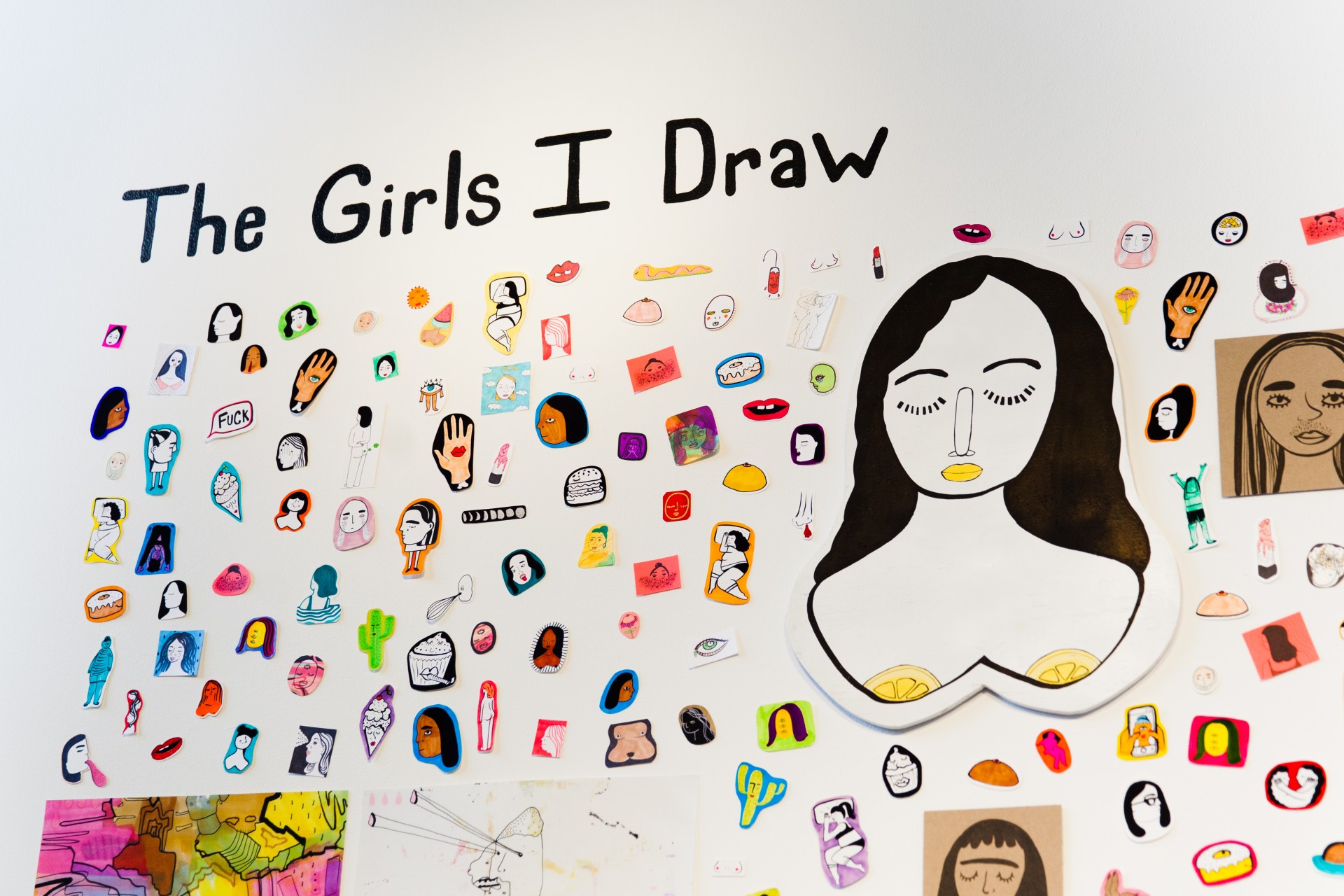 White gallery wall with collaged assortment of stickers, paintings and drawings. Text reads, "The Girls I Draw"