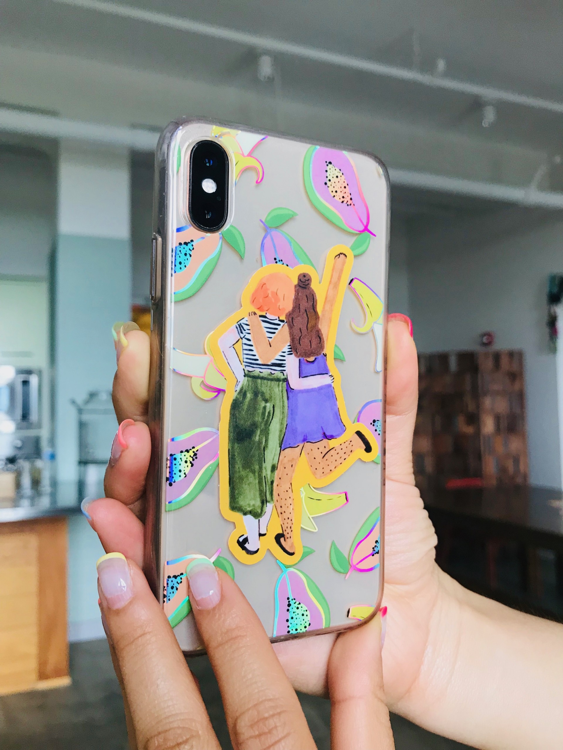 A sticker of two girls with their hands around each other with their back towards the viewer placed on an iphone 