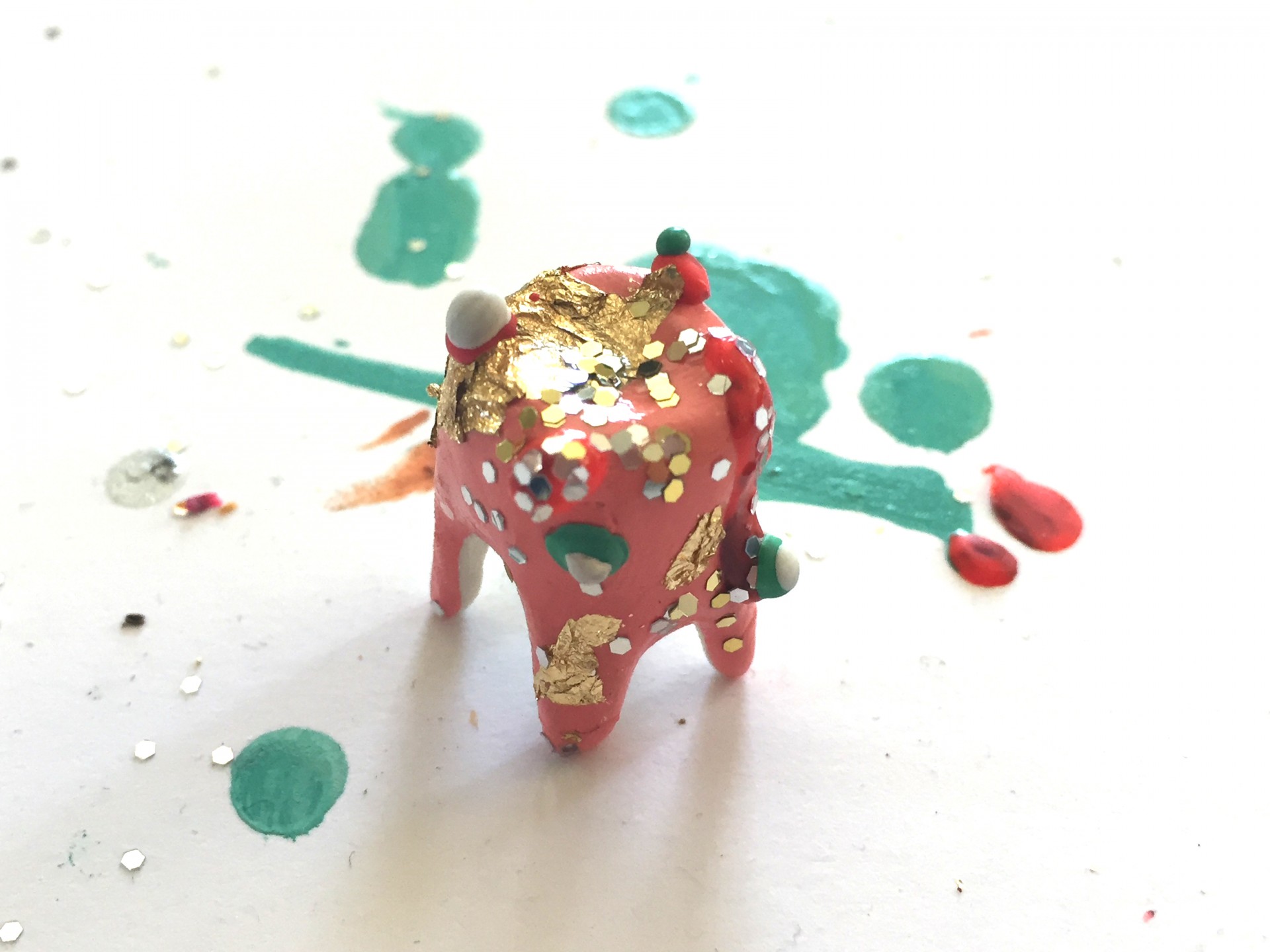 Single clay tooth covered in pink paint pen, colorful wax droplets and gold glitter. 