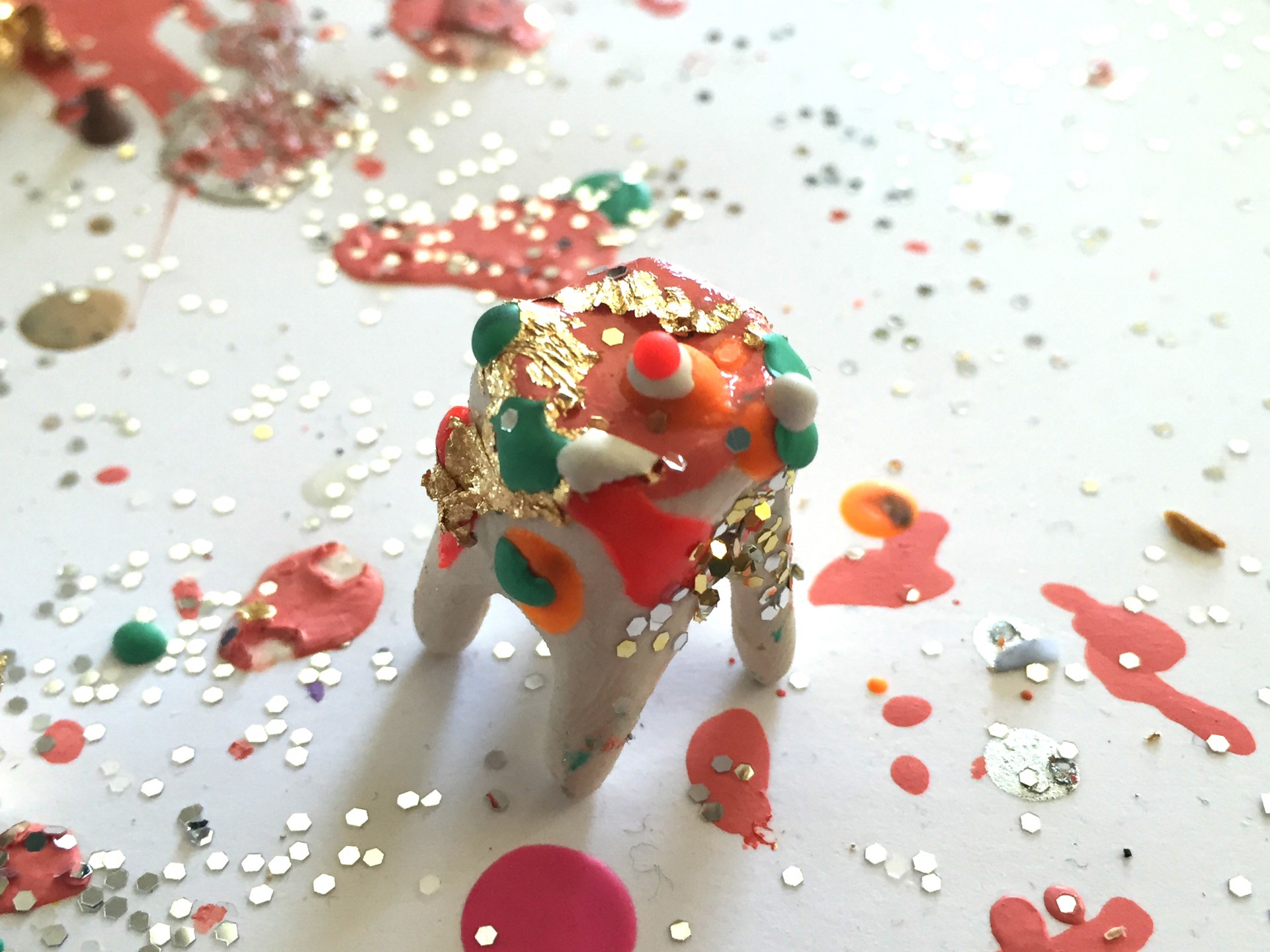 Single clay tooth covered in pink paint pen, colorful wax droplets and gold glitter. 