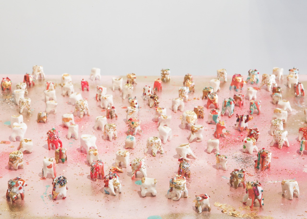 Large collection of small clay teeth decorated in marker, paint and crayon wax on pink surface in gallery setting. 